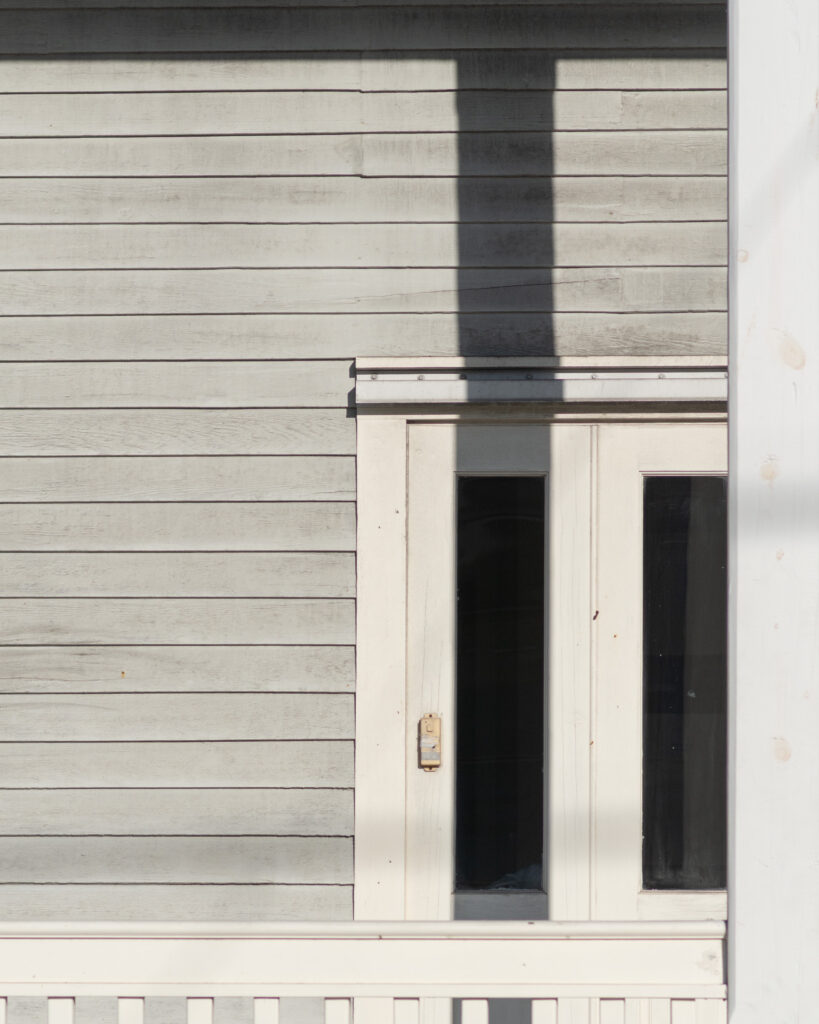 “White wooden siding with a window partially in shadow, showing subtle surface wear.”