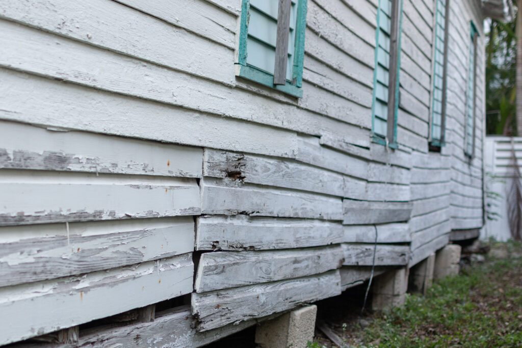 “Weathered wooden siding with warped and displaced boards indicating structural shift.”
