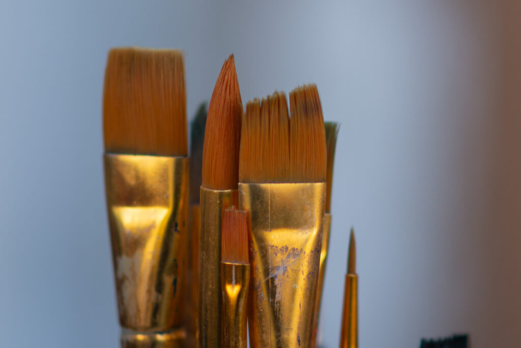 “Paintbrushes with worn bristles and brass ferrules standing upright.”